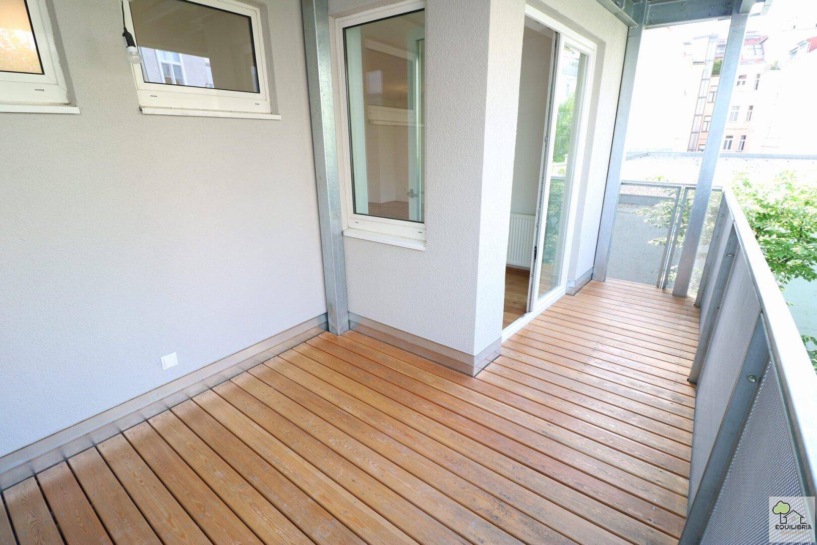 Geräumiger Balkon mit Holzboden und Metallgeländer, ideal für entspannte Stunden im Freien mit Blick ins Grüne.