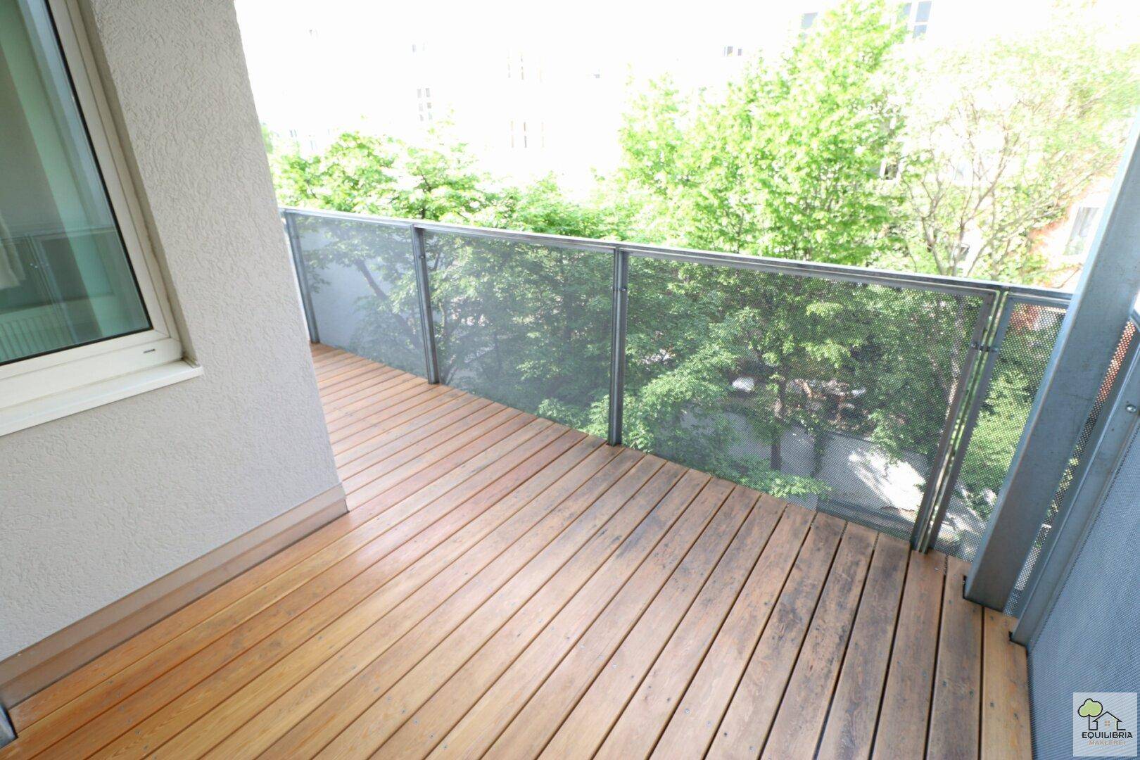 Heller Balkon mit Holzboden und Blick ins Grüne, ideal zum Entspannen.