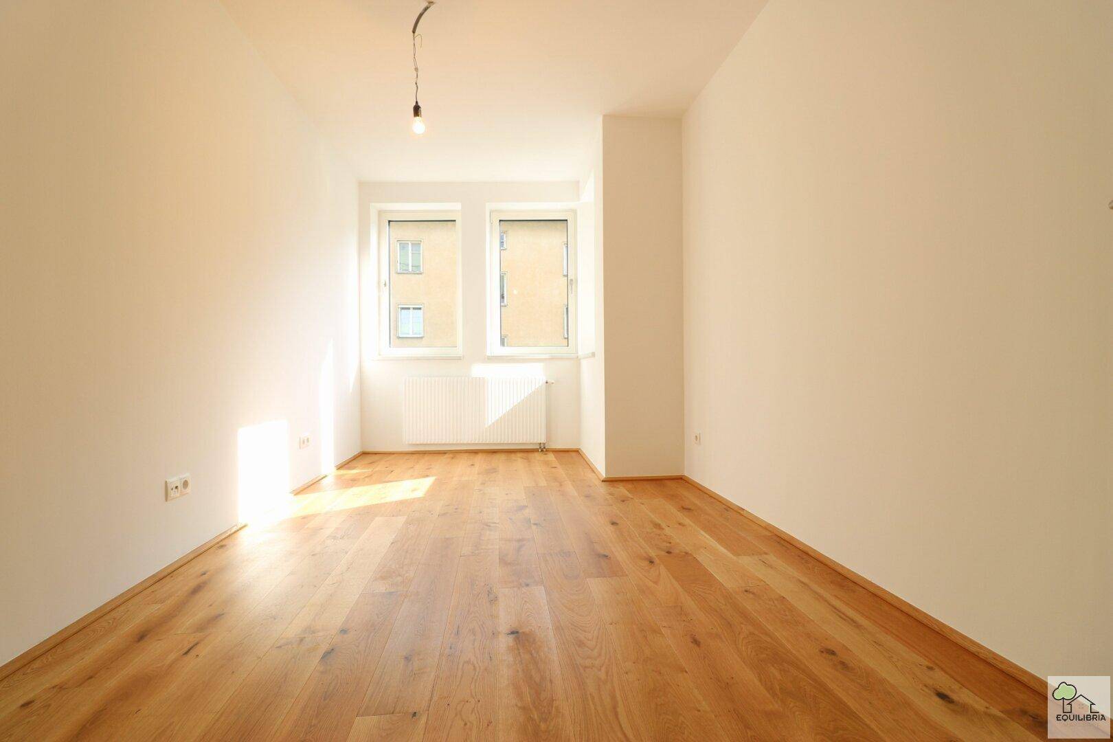 Lichtdurchfluteter Raum mit hellem Holzboden und großen Fenstern, bereit zur Einrichtung.