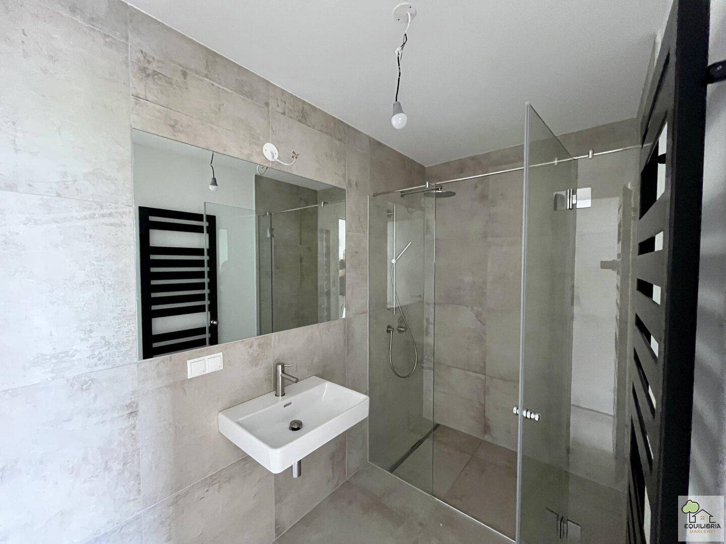 Modernes Badezimmer mit ebenerdiger Dusche, Waschbecken und beheiztem Handtuchhalter.