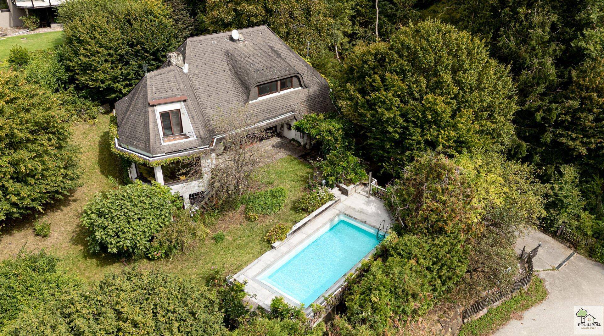 Luftaufnahme eines charmanten Hauses mit privatem Swimmingpool, eingebettet in eine grüne, bewaldete Umgebung.