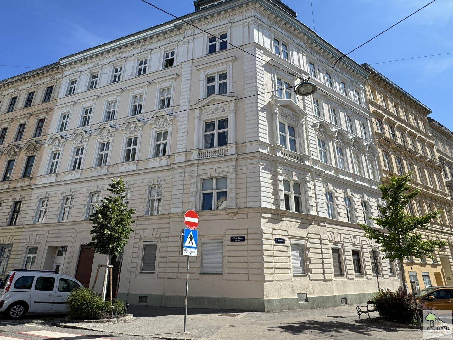 Historisches Eckgebäude mit klassischer Fassade und vielen Fenstern in einer städtischen Umgebung.