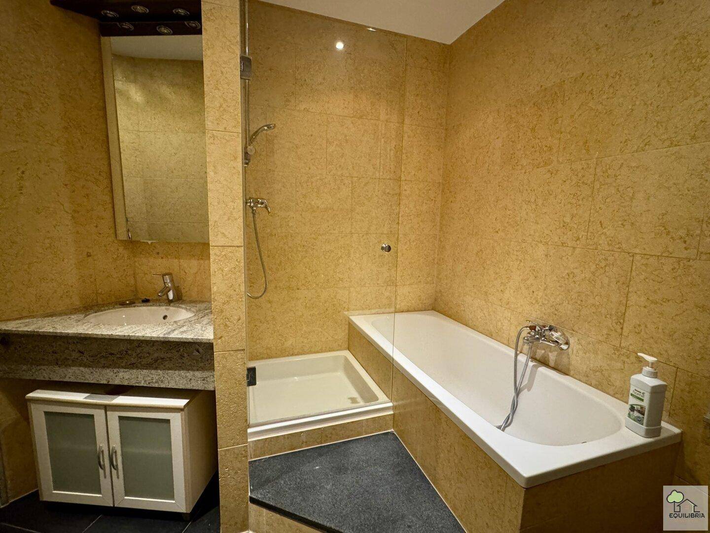 Badezimmer mit Badewanne, Duschkabine und Einzelwaschbecken, komplett gefliest in warmen Erdtönen.