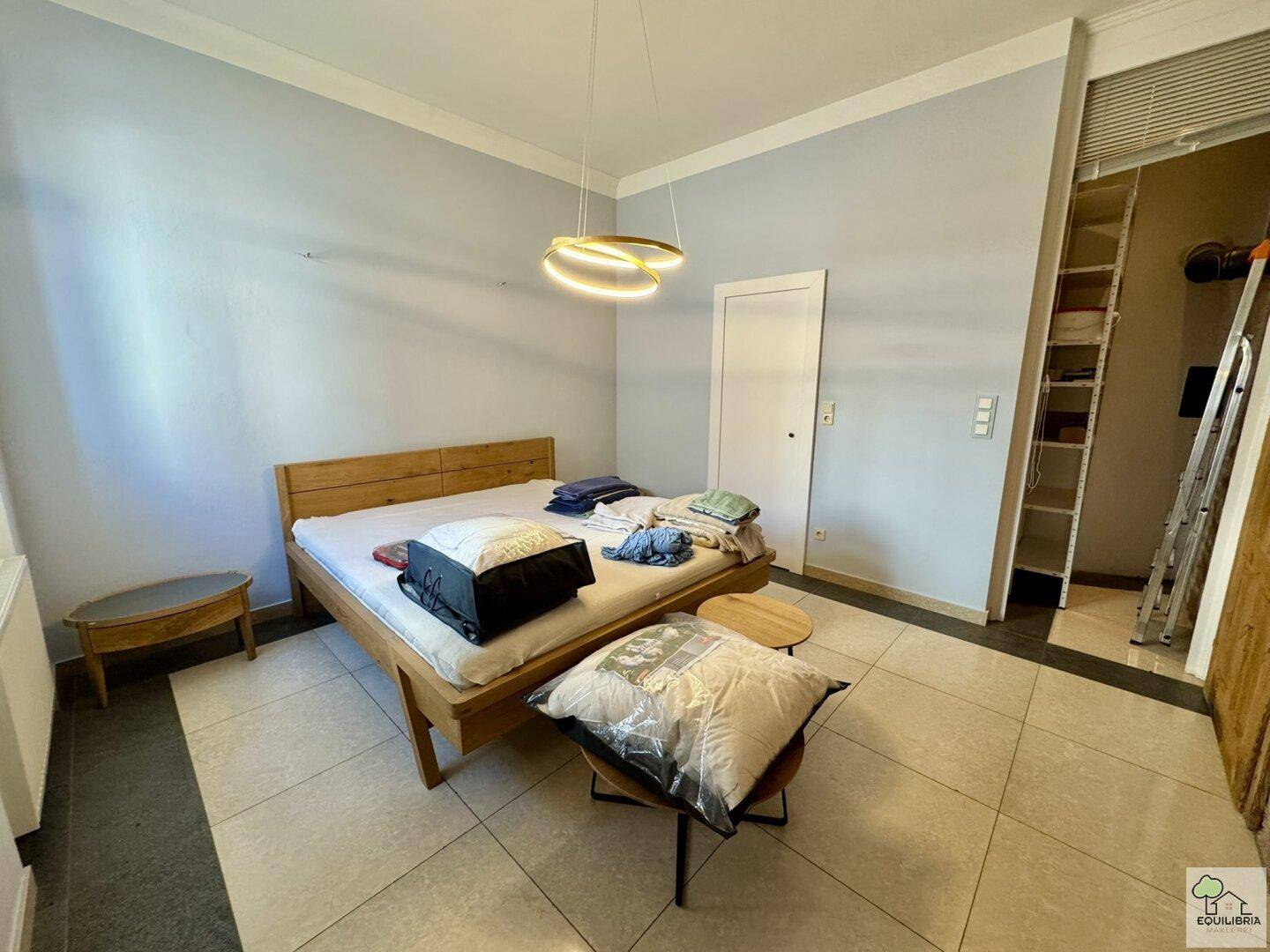 Schlafzimmer mit Holzbett, hellem Fliesenboden und offenem Regalsystem für Kleidung und Ablage.