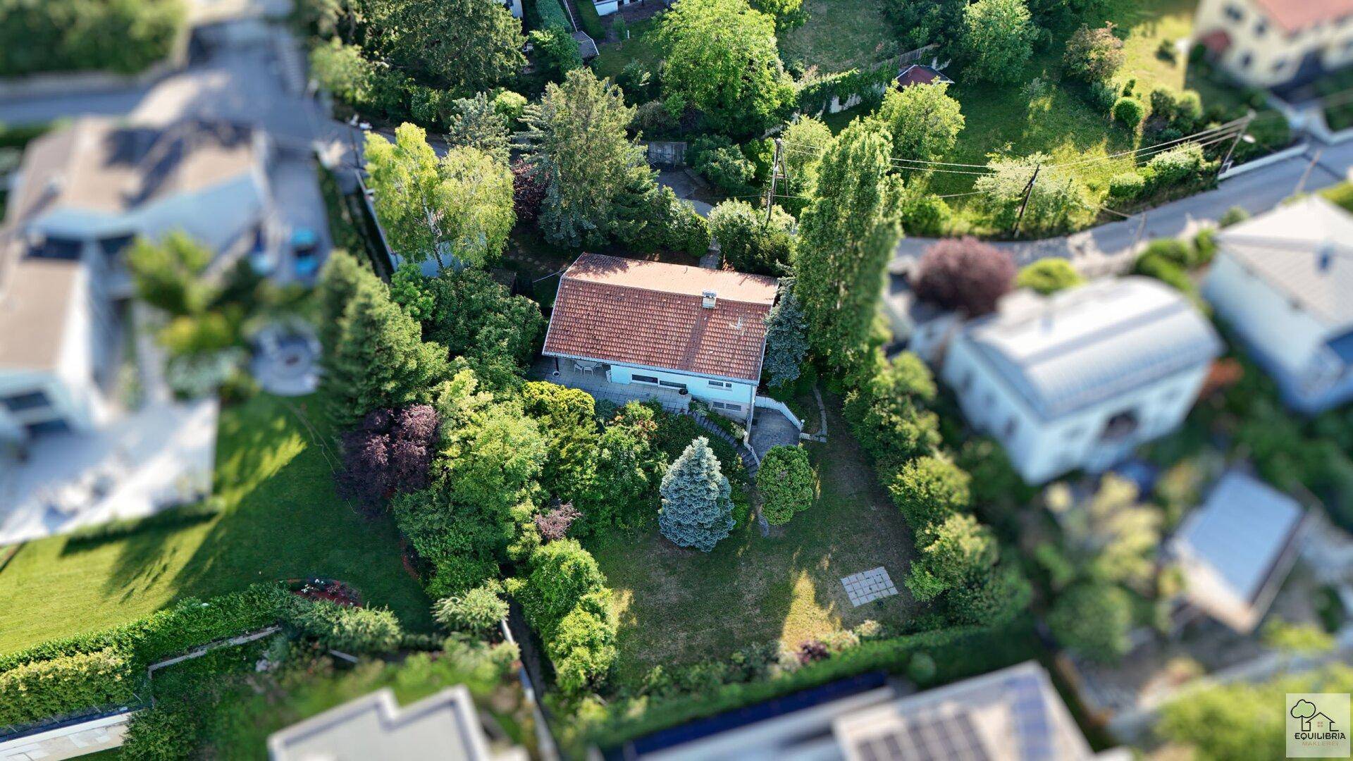 Haus mit hellblauer Fassade und rotem Ziegeldach, umgeben von einem gepflegten Garten mit Rasen und Bäumen.