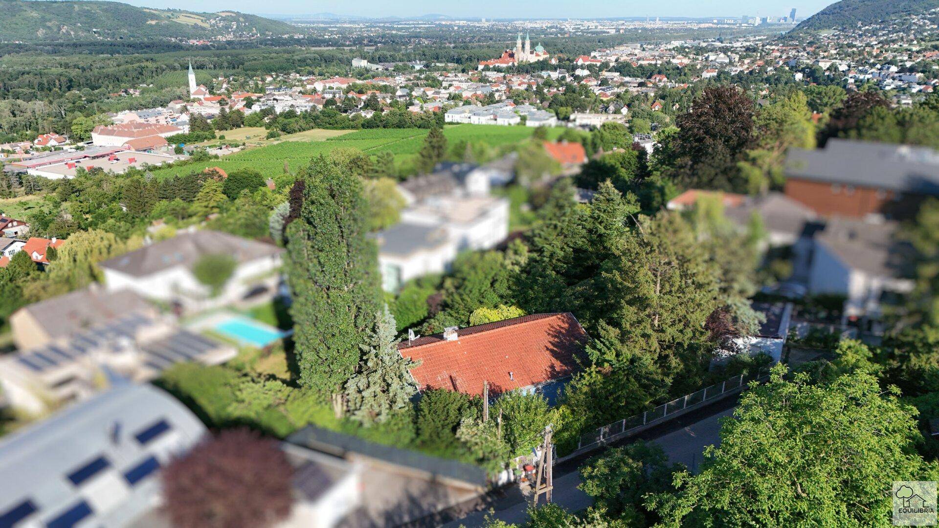 Luftaufnahme eines Wohnviertels mit einem Haus im Grünen und Blick auf die entfernte Stadt.