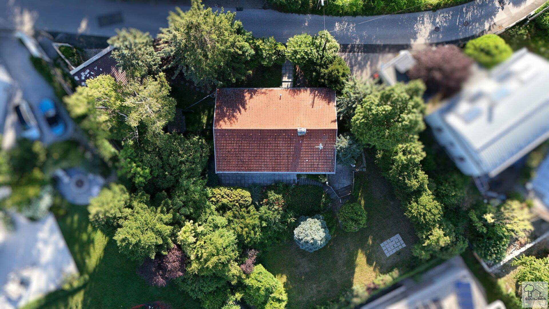 Oberansicht eines Hauses mit rotem Ziegeldach, umgeben von üppigem Grün und Bäumen.