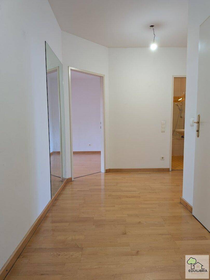 Geräumiger Flur mit hellem Holzparkettboden und einem großen Wandspiegel.