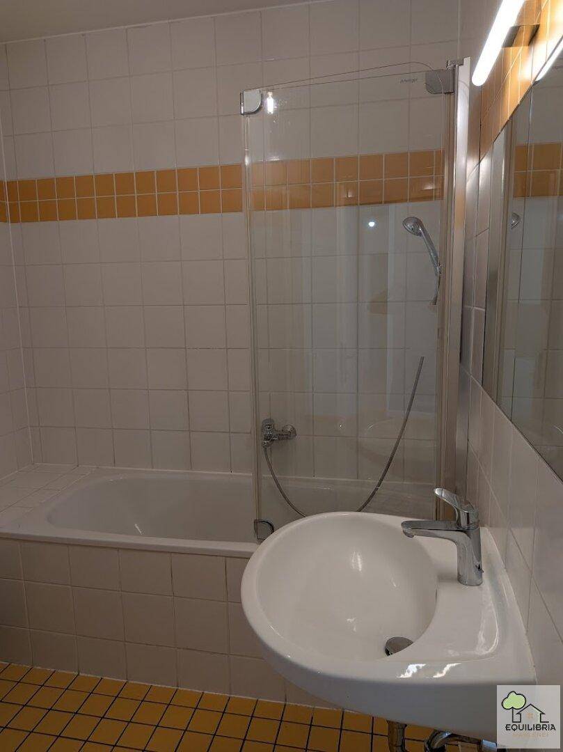 Badezimmer mit Badewanne, Waschbecken und weißen Fliesen mit gelbem Akzentstreifen.