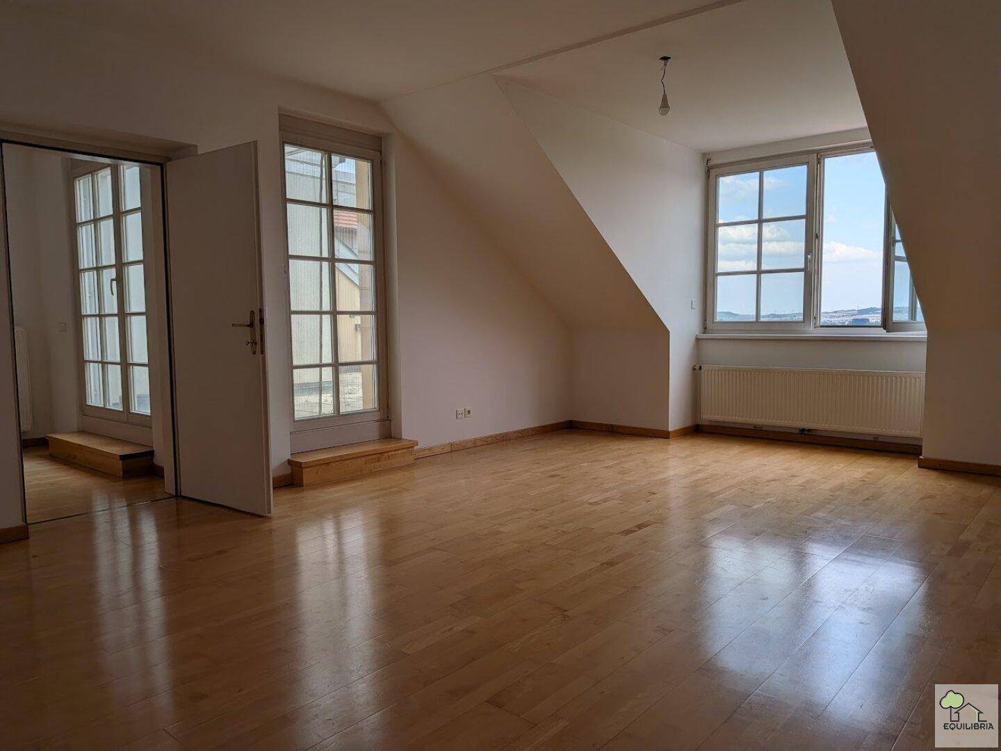 Geräumiges Dachgeschosszimmer mit Holzparkettboden, großen Fenstern und schrägen Wänden.
