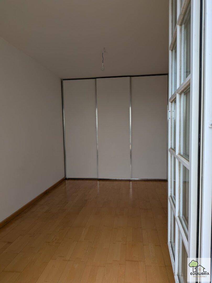Helles Zimmer mit Holzparkettboden und praktischen Einbauschränken entlang einer Wand.