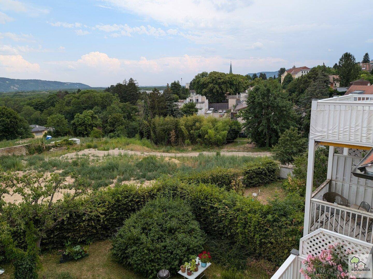 Weitläufiger Ausblick von einem Balkon über eine grüne Landschaft und die Dächer der Stadt.