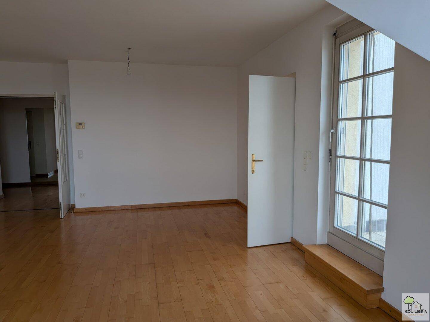 Heller, leerer Raum mit Holzparkettboden und Zugang zu einer Außenterrasse.