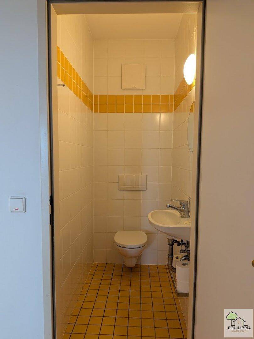 Kleines Gäste-WC mit Toilette, Waschbecken und gelb-weiß gefliestem Boden und Wänden.
