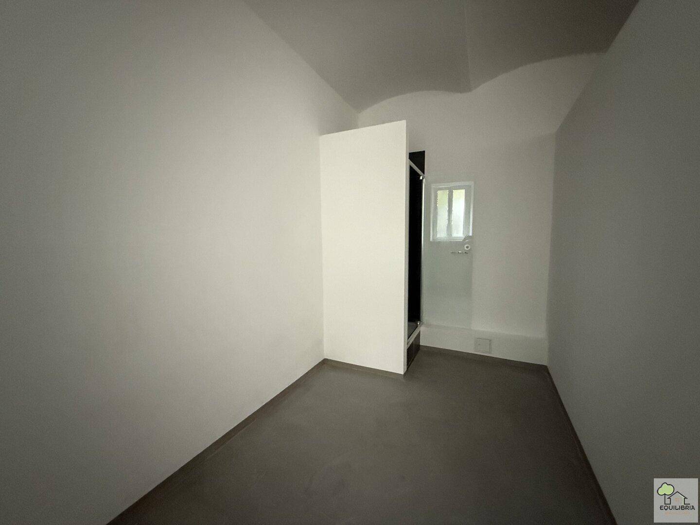 Kleiner, leerer Raum mit dunklem Boden und einem Fenster, bietet einfache Nutzung.
