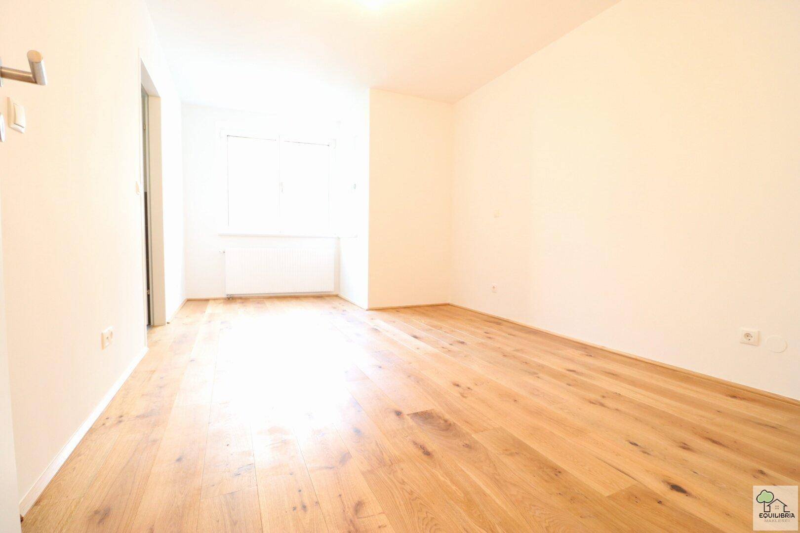 Helles, leeres Zimmer mit neuem Holzparkettboden und weißen Wänden, bereit zum Einzug.