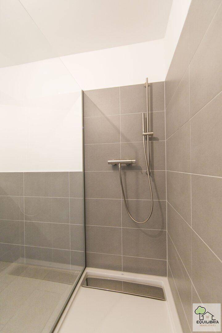 Detaillierte Ansicht einer modernen, gefliesten Dusche mit Duschrinne und Glasabtrennung.