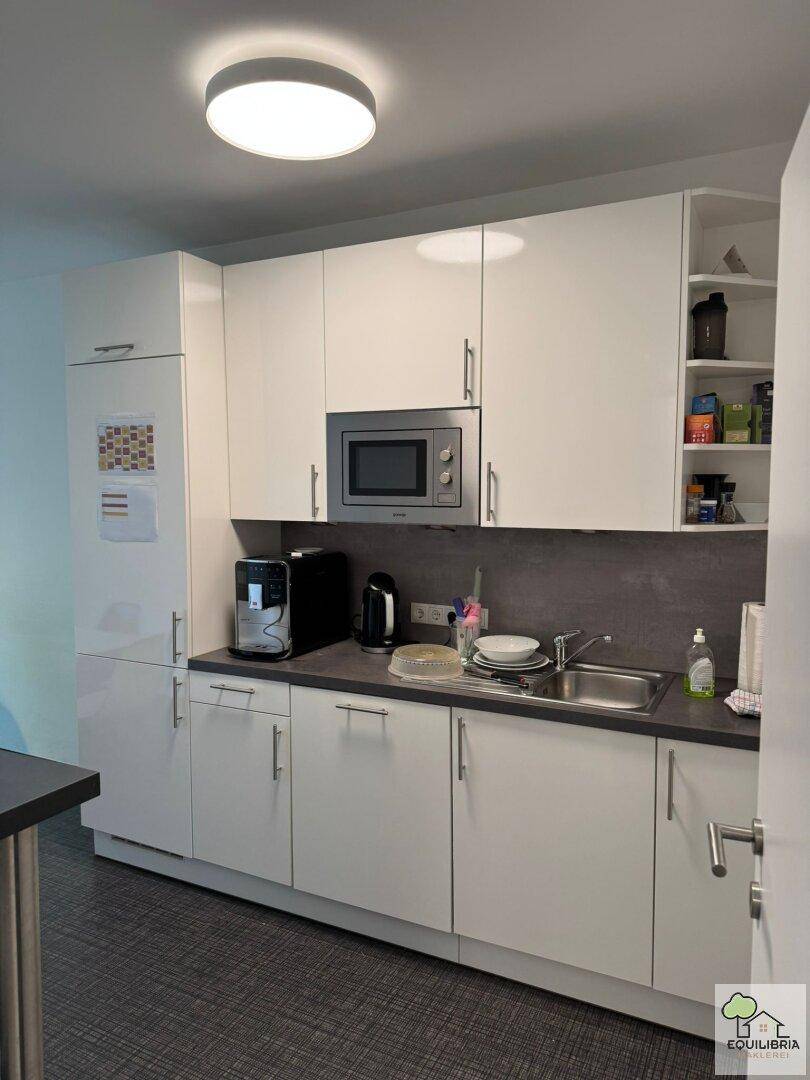 Detailansicht der modernen weißen Büroküche mit Mikrowelle, Kaffeemaschine und Spülbecken.