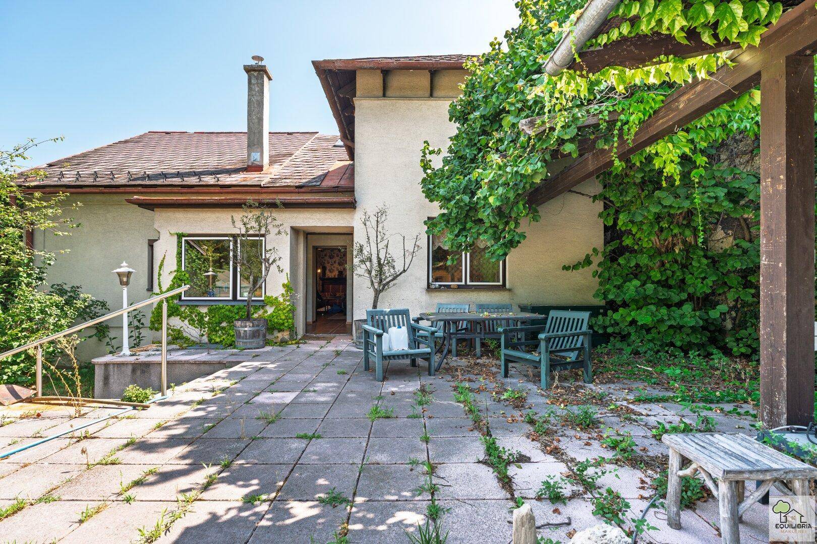 Gepflasterte Terrasse mit Gartenmöbeln und üppiger Begrünung am Haus.