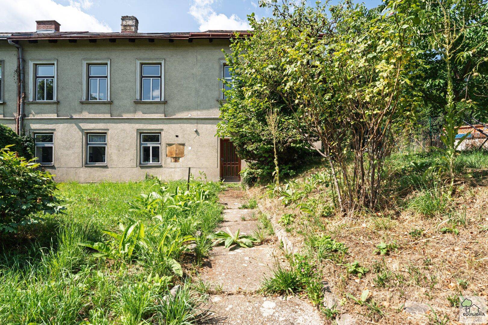 Fassade eines älteren Gebäudes mit einem zugewachsenen Pfad und viel Vegetation.