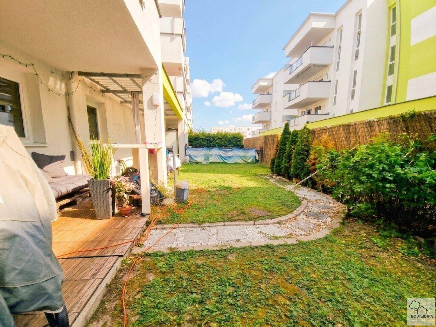 Gemütliche Holzterrasse mit Sitzgelegenheiten und Blick auf den privaten Gartenbereich eines Neubaus.