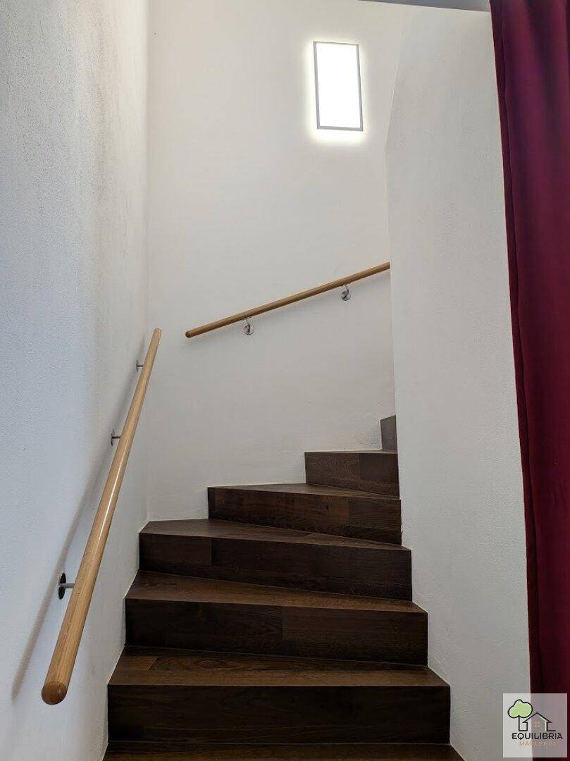 Holztreppe mit hellem Geländer, die die verschiedenen Etagen des Hauses verbindet.