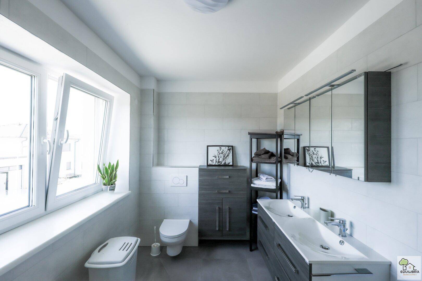 Modernes Badezimmer mit Doppelwaschbecken, Wand-WC und großem Fenster.