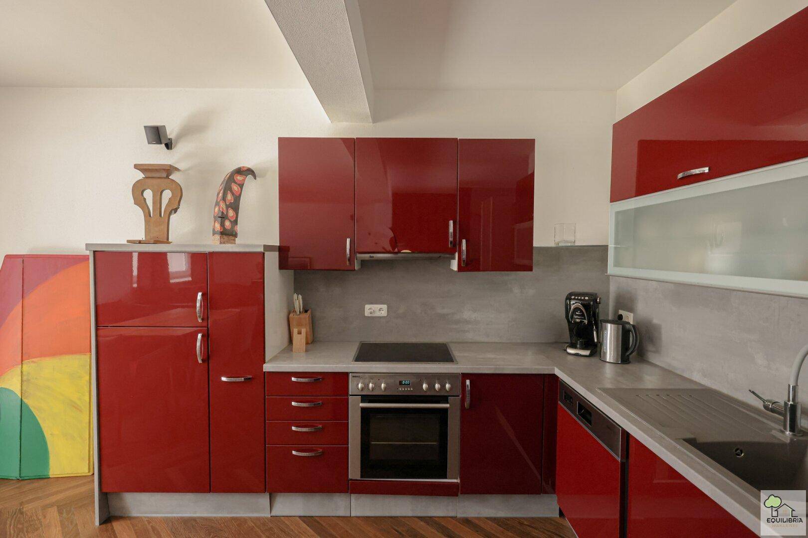 Moderne Küche mit roten Hochglanzfronten, integrierten Geräten und Holzboden.