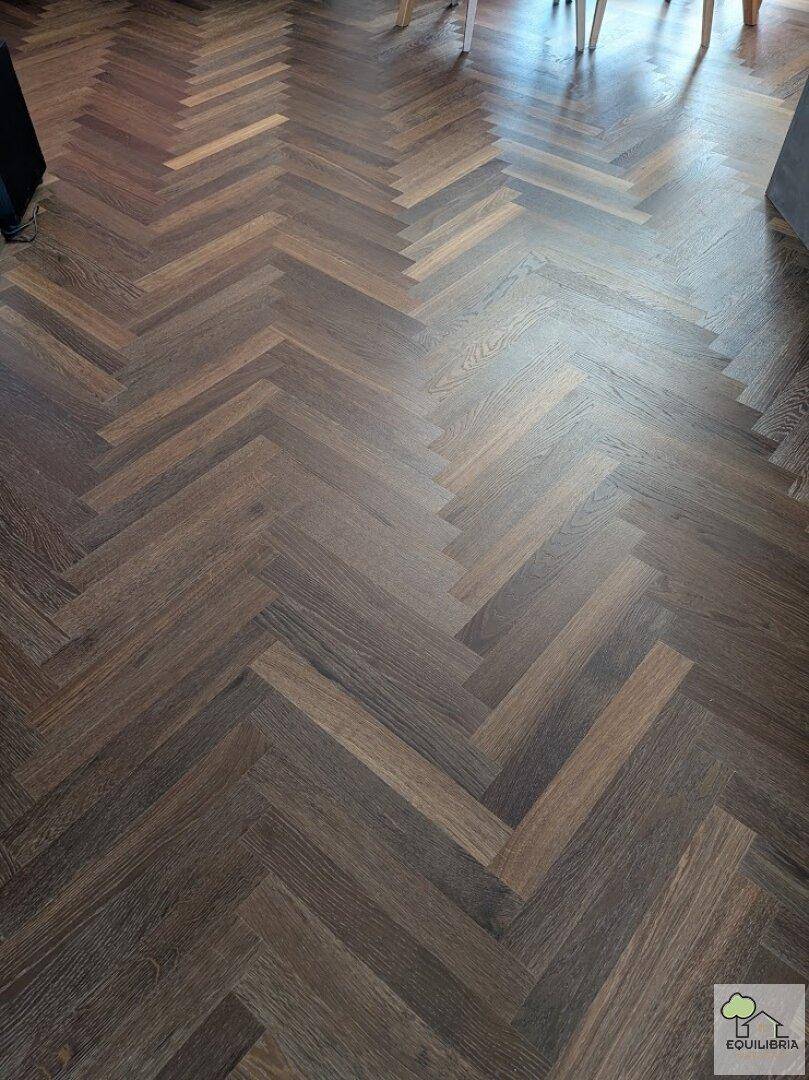 Detailaufnahme des Fischgrätparkettbodens in dunklem Holzton.