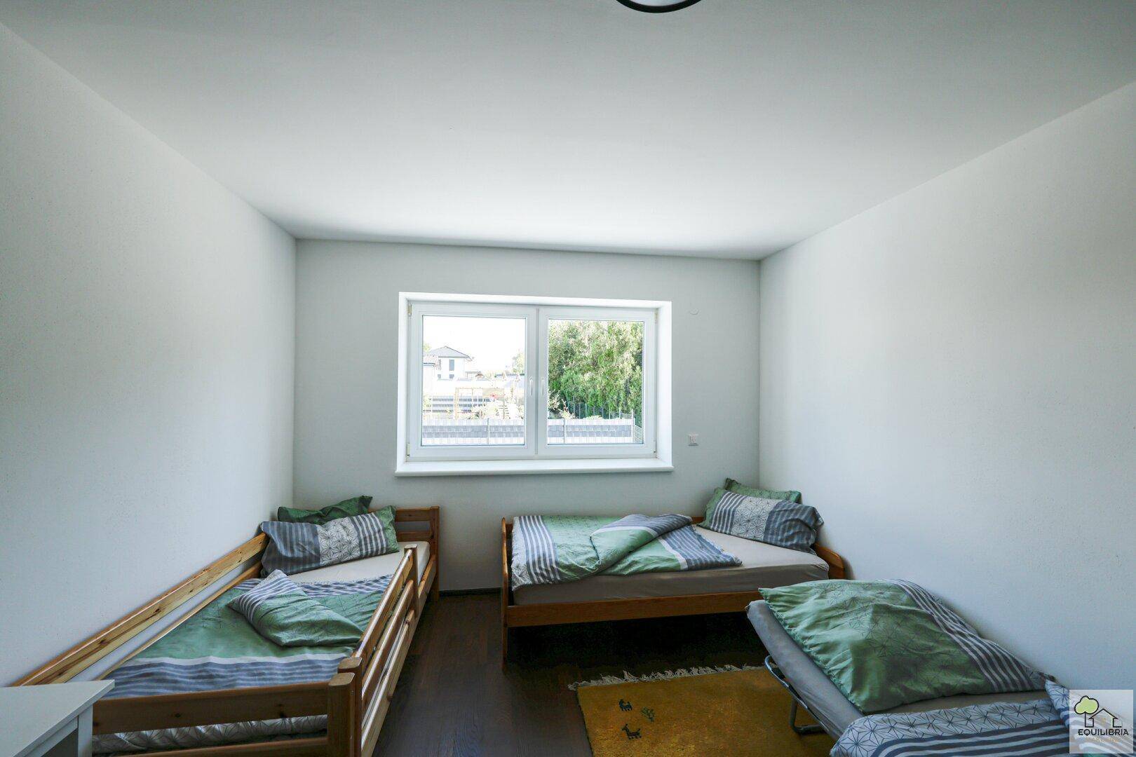 Helles Kinderzimmer mit zwei Betten und Fenster mit Blick nach draußen.