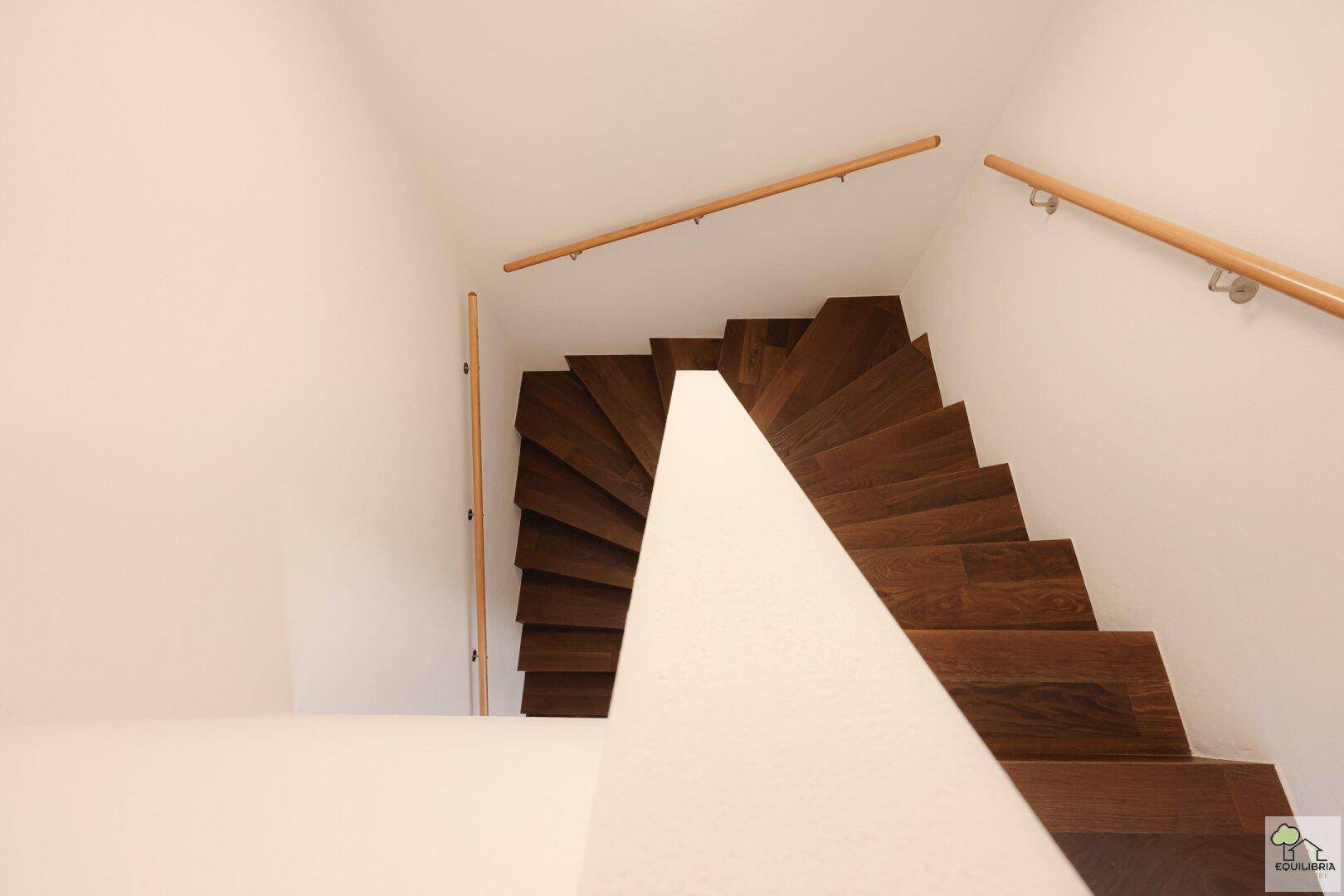 Wendeltreppe aus Holz mit hellem Geländer, die die oberen Etagen erschließt.