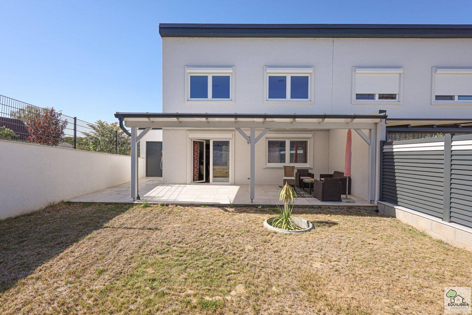 Gartenbereich mit Rasenfläche, überdachter Terrasse und Zugang zum Haus.