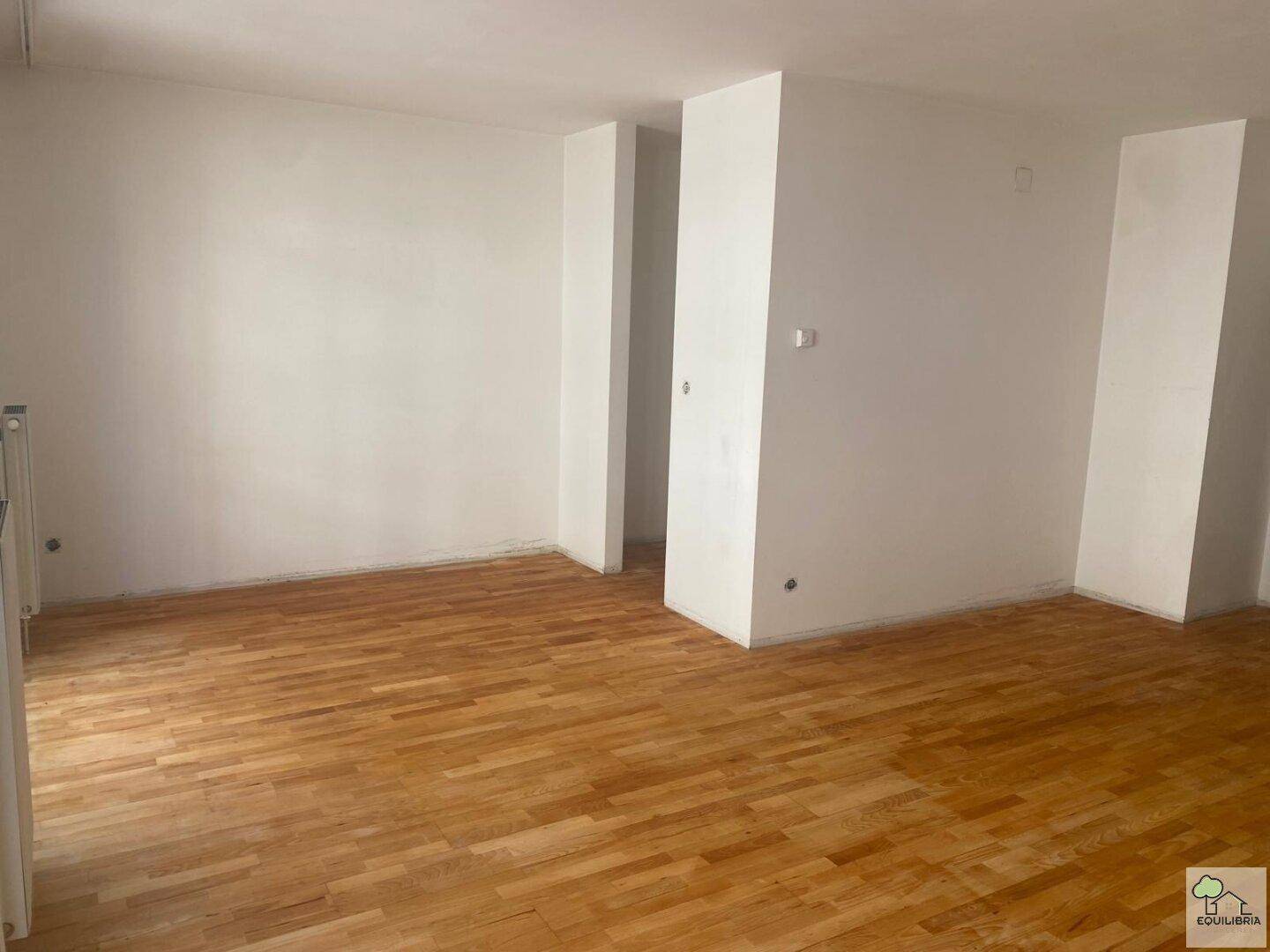 Geräumiger, leerer Raum mit hellem Parkettboden und weißen Wänden, bereit zur individuellen Gestaltung.