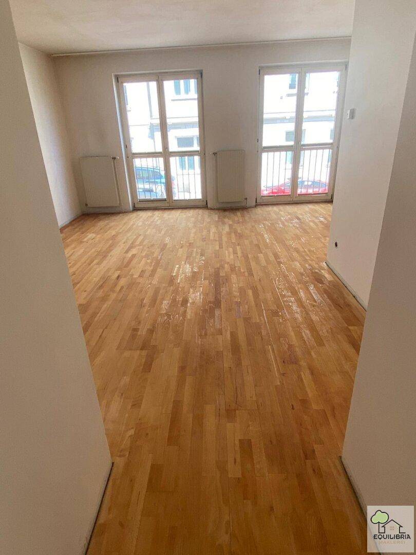 Geräumiges Wohnzimmer mit Parkettboden und Zugang zu französischen Balkonen, hell und einladend.