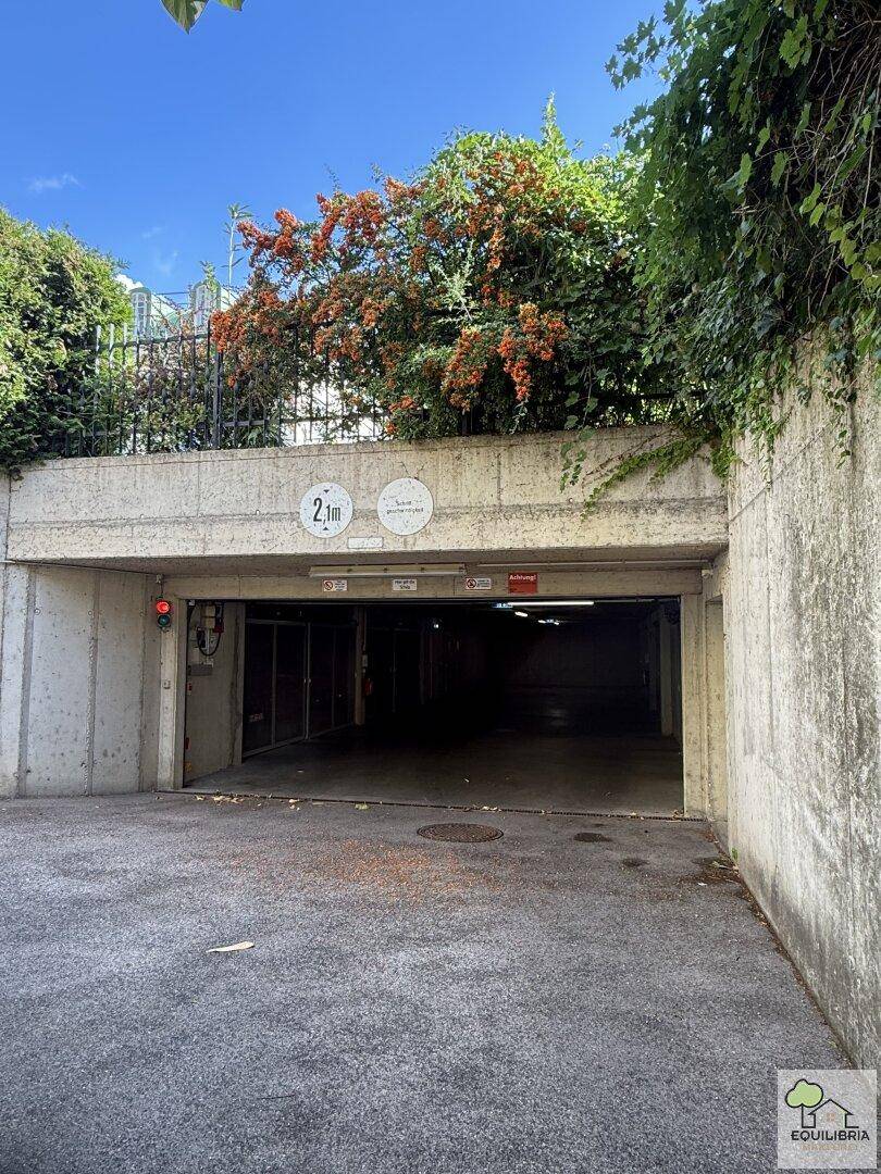 Eingang zur Tiefgarage mit Höhenbegrenzung von 2,1 Metern, umgeben von Pflanzen und Betonwänden.