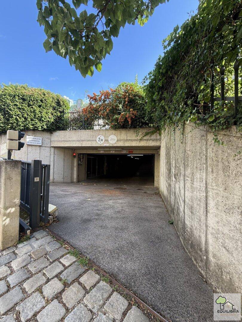 Einfahrt zur Tiefgarage mit Betonwänden, umgeben von üppigem Grün und Kopfsteinpflaster.