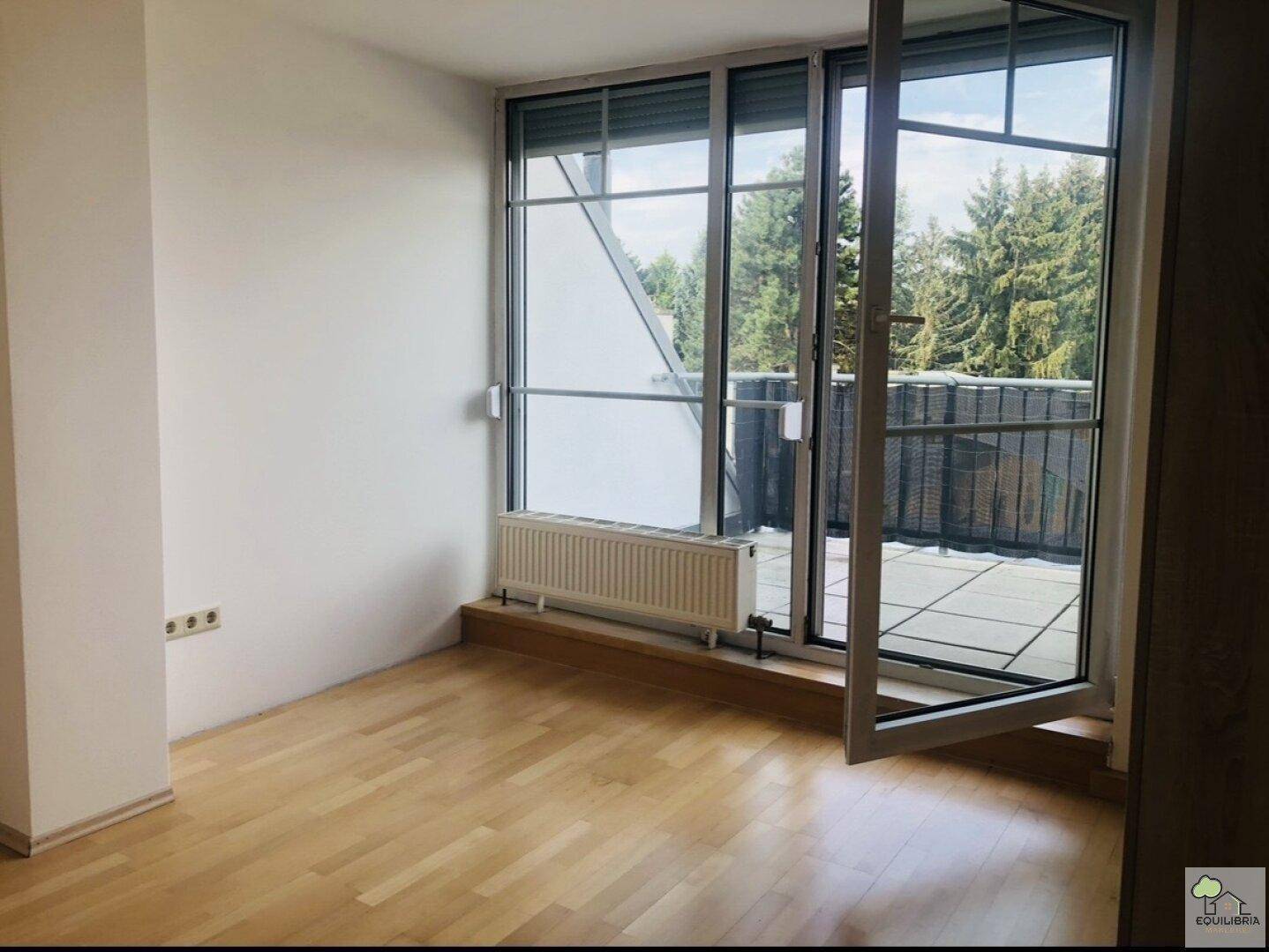 Heller Raum mit Zugang zu einem Balkon oder einer Terrasse und Blick ins Grüne.
