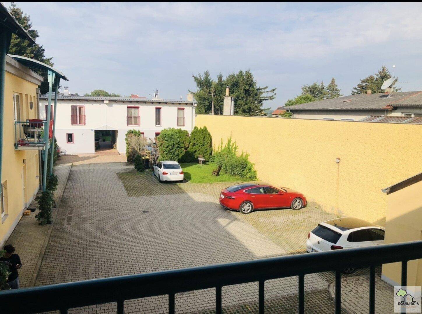 Innenhof mit Parkplätzen, umgeben von Gebäuden und einer markanten gelben Mauer.