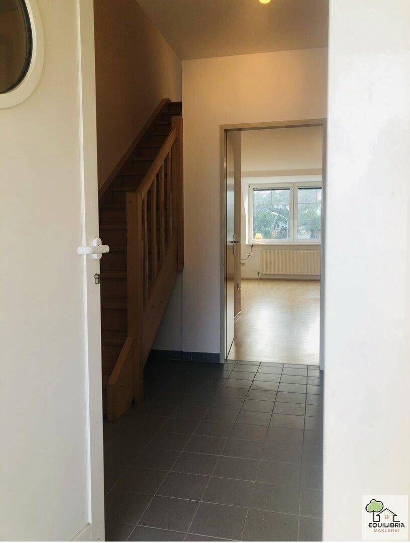 Heller Flur mit Holztreppe und Fliesenboden, der zu einem weiteren Zimmer führt.