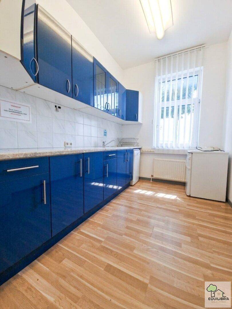 Moderne Küche mit glänzenden blauen Schränken, weißem Fliesenspiegel und hellem Holzfußboden.