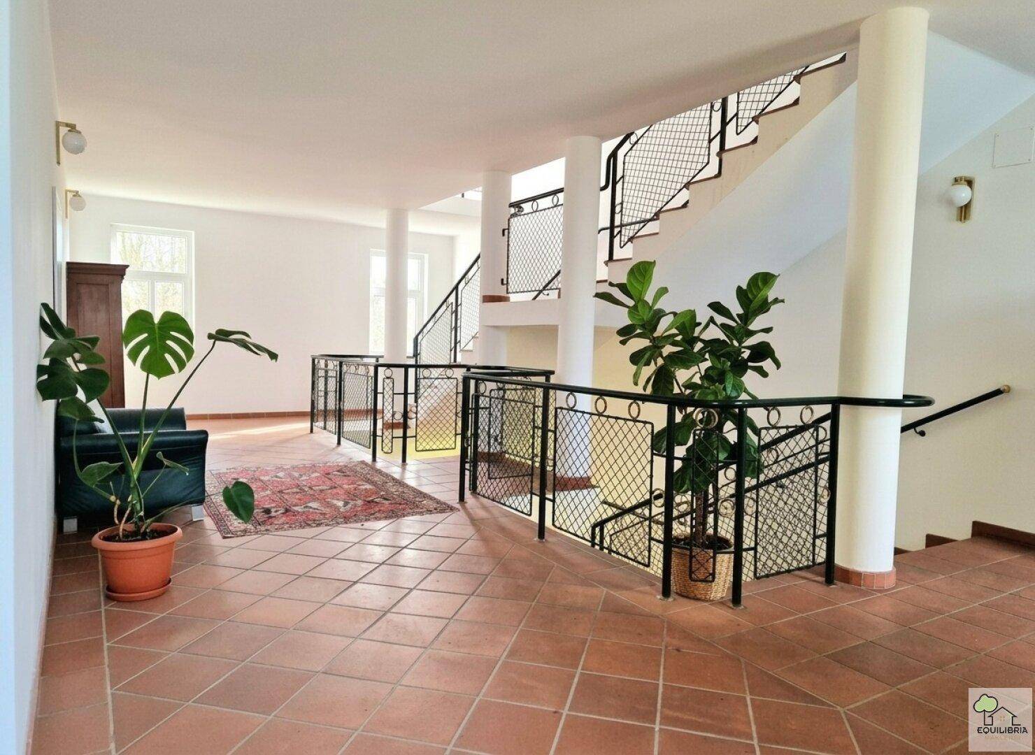 Geräumiger Flur mit Terrakottafliesen, Säulen und einer Treppe mit schmiedeeisernem Geländer.
