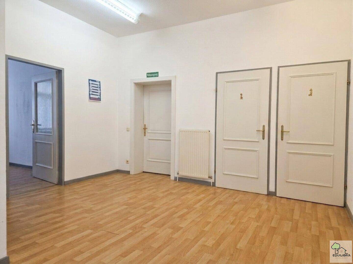 Flur mit hellem Parkettboden und mehreren Türen, darunter ein Ausgangsschild.