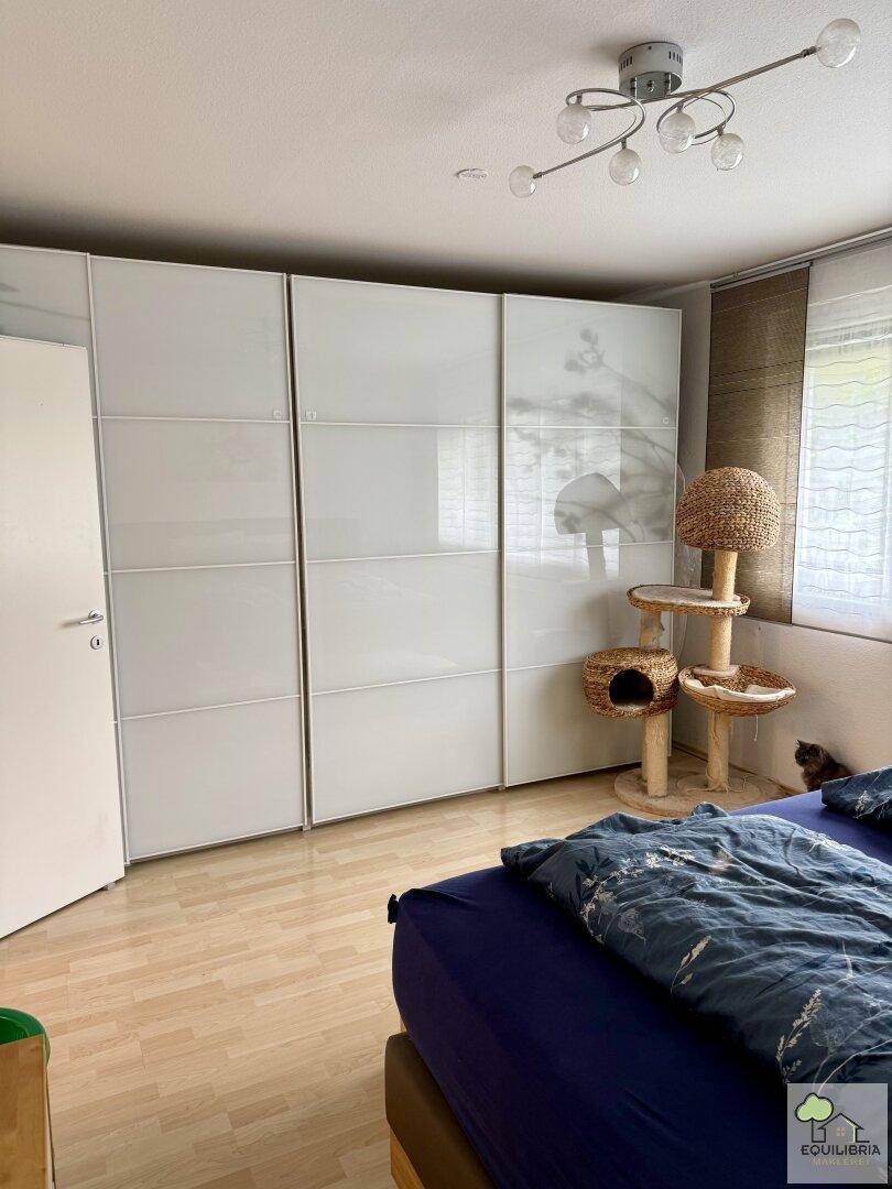 Schlafzimmer mit großen weißen Schiebetürenschränken, Holzboden und einem Katzenbaum am Fenster.