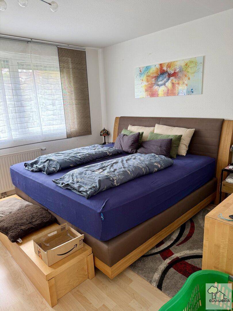 Helles Schlafzimmer mit großem Bett, Holzboden und einem farbenfrohen Kunstwerk an der Wand.