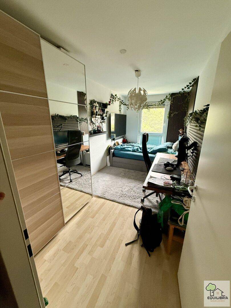 Geräumiges Schlafzimmer mit Spiegelschränken, Holzboden und Teppichbereich, kombiniert mit einem Arbeitsplatz.