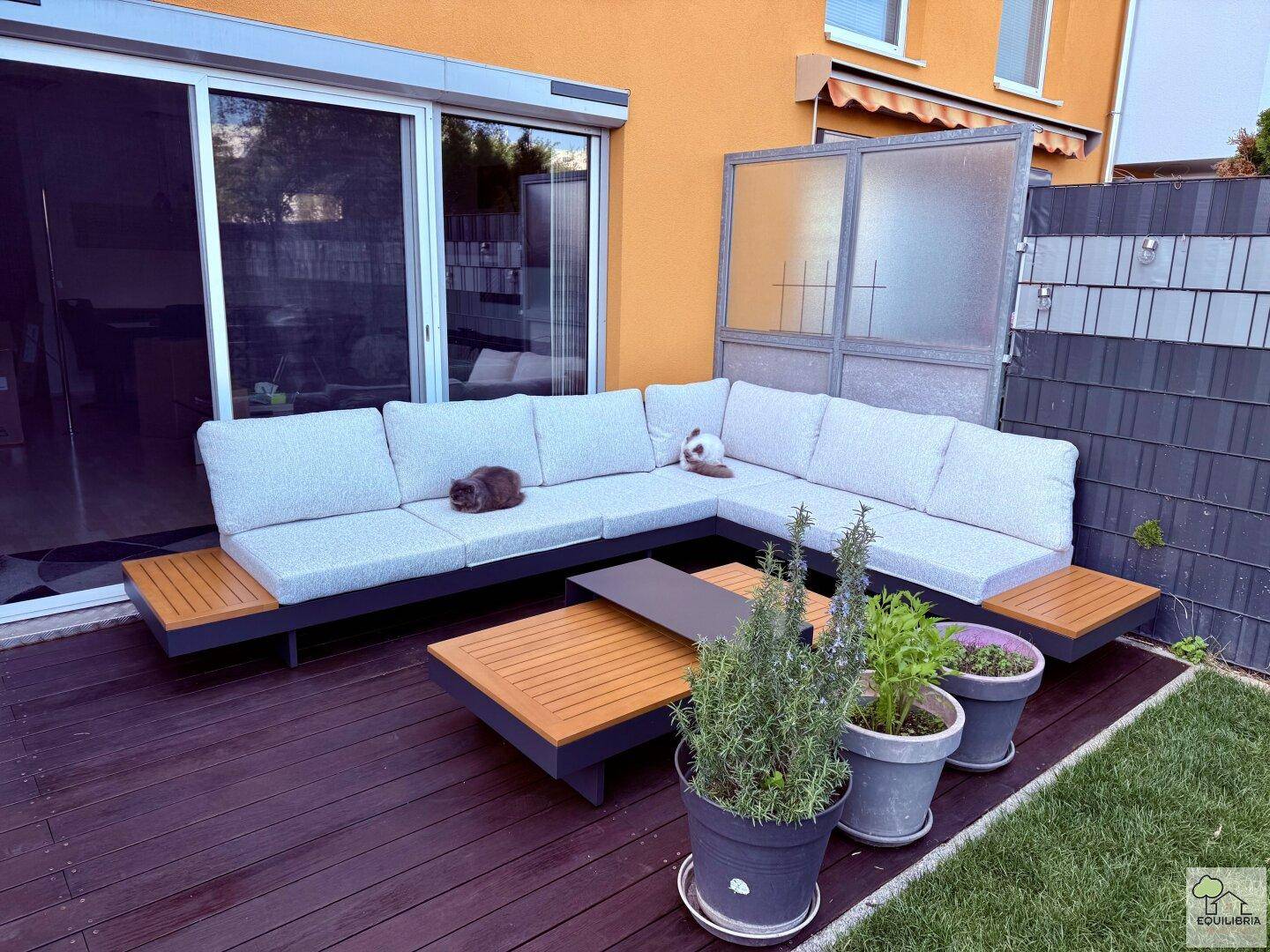 Gemütliche Terrasse mit großem L-förmigem Sofa, Holzboden und Pflanzen, ideal zum Entspannen im Freien.