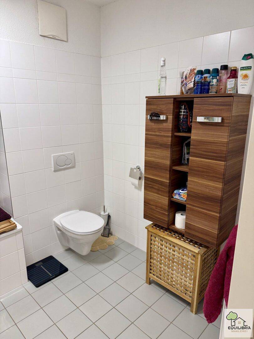 Modernes Badezimmer mit weißen Fliesen, wandhängendem WC und einem Holzschrank für Stauraum.