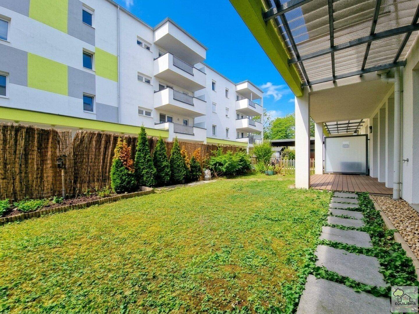 Weitläufiger Gartenbereich mit Rasen und Trittsteinen, umgeben von einem modernen Wohnkomplex.