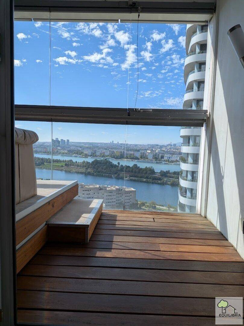 Gemütlicher Balkon mit Holzboden und Sitzgelegenheit, bietet Panoramablick auf Stadt und Fluss.