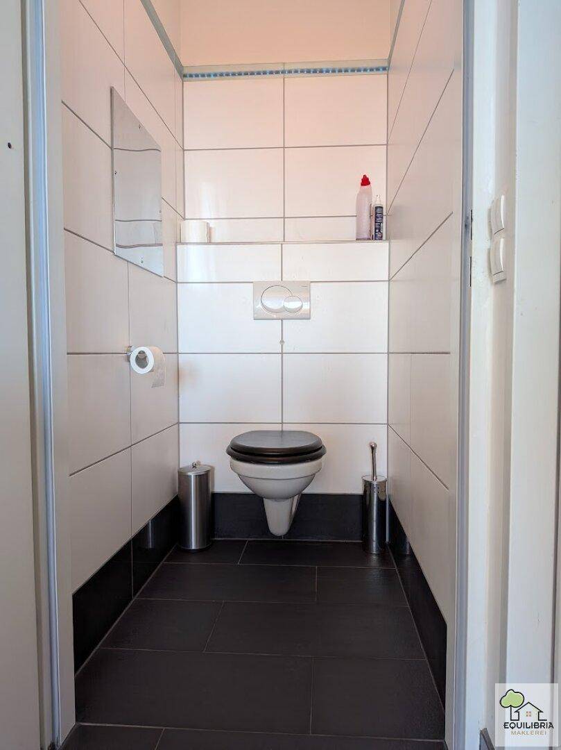 Separates WC mit Wand-WC und dunklen Bodenfliesen in minimalistischem Design.